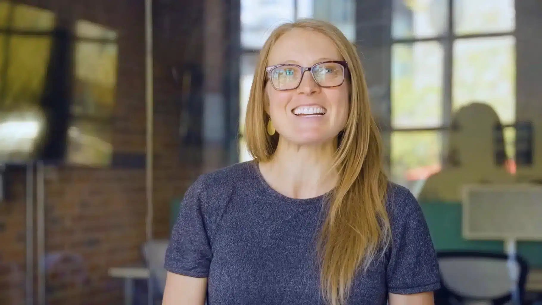 Closeup of white redheaded woman wearing glasses and smiling in a conference room.