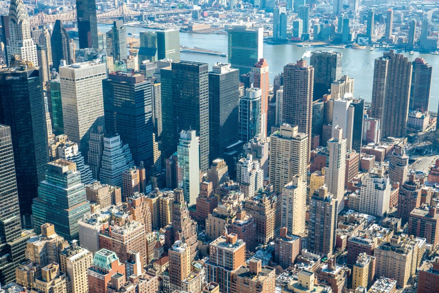 Aerial view of a dense cityscape with diverse skyscrapers and buildings. The river in the background adds depth, depicting a vibrant urban environment.