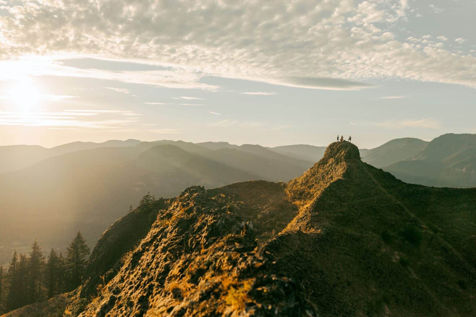 Three very small figures on a mountain peak near golden hour.